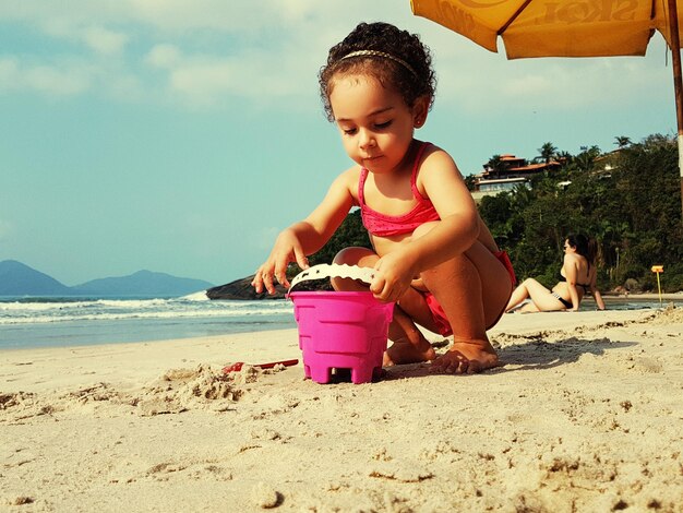 Girl playing on sand at beach against sky