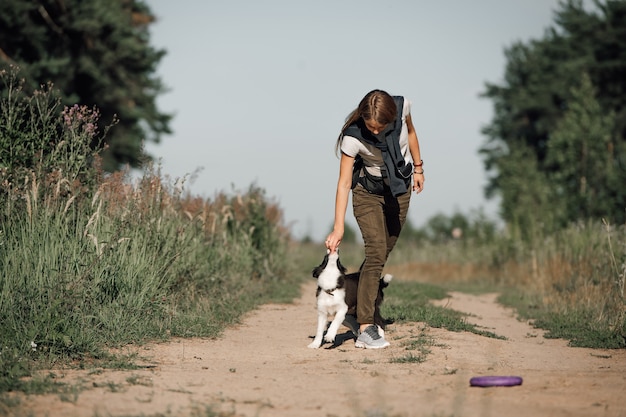 Girl playing with black and white border collie dog puppy on the forest path