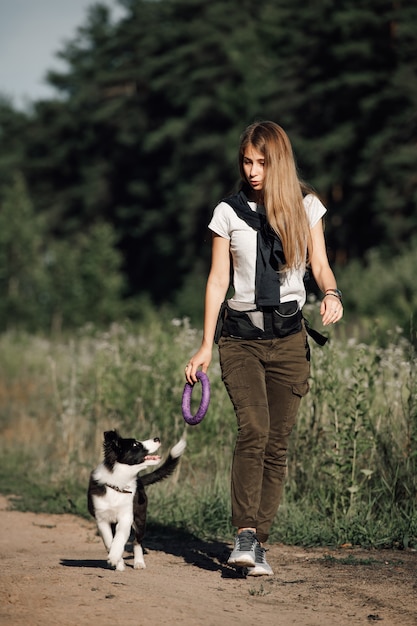 Ragazza che gioca con il cucciolo di cane border collie bianco e nero sulla strada forestale