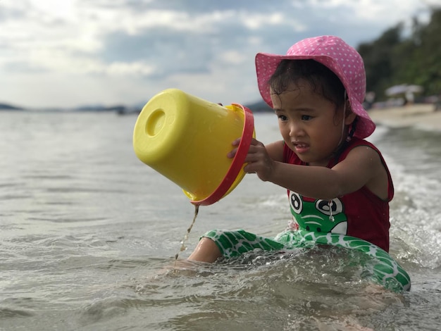 写真 ビーチに座っている女の子がバケツで遊んでいる