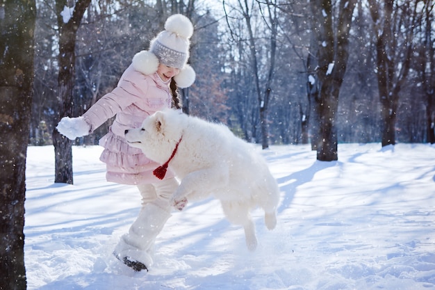 クリスマスの朝に雪に覆われた公園でサモエドの子犬と遊ぶ女の子