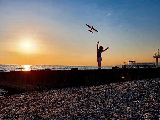 Foto ragazza che gioca con un aereo giocattolo sulla spiaggia durante il tramonto