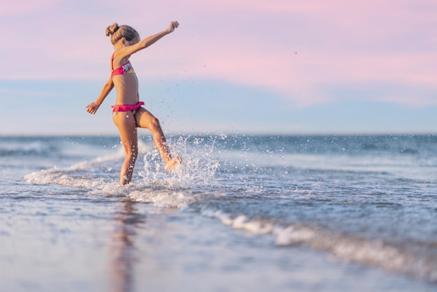 休暇を楽しんでいる夏の太陽の下で蹴ったり回転したりする波で遊ぶ女の子