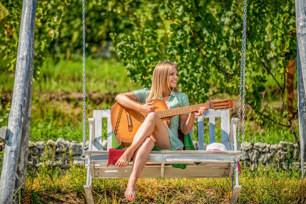 Девушка играет на гитаре в парке на скамейке. Молодая женщина любит играть на гитарах.