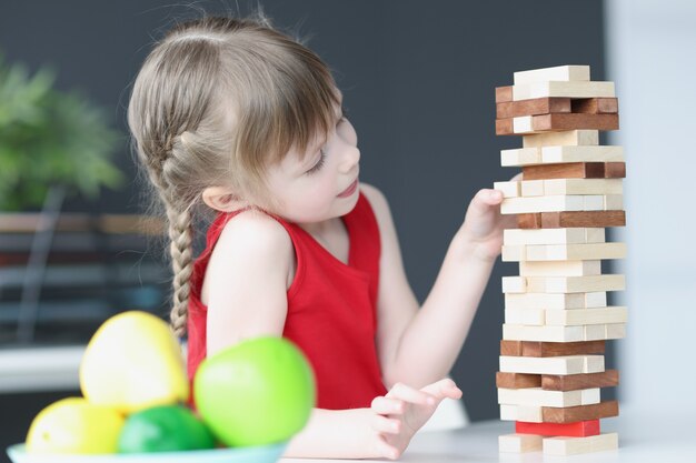 Girl plays and takes out wooden blocks from tower. Educational games for children concept