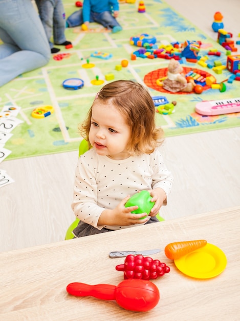 La ragazza gioca con gli articoli per la casa dei bambini e la frutta artificiale a tavola. utensili da cucina