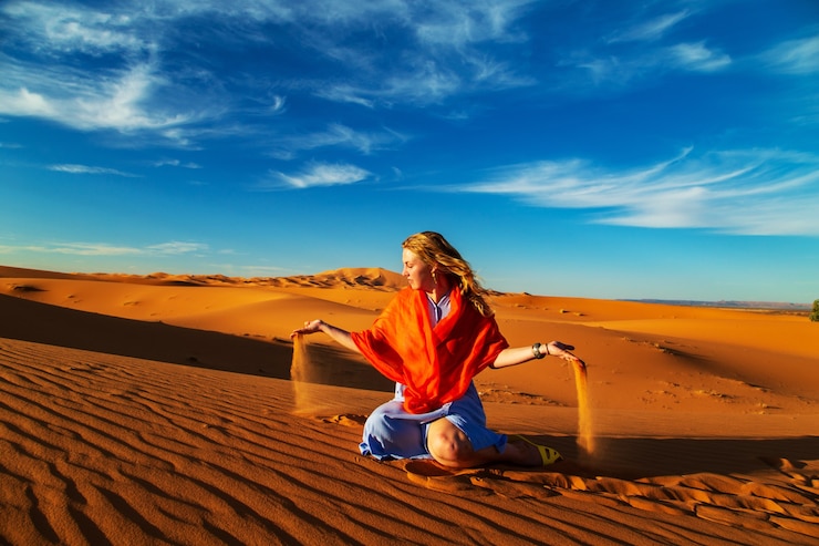 Girl plays with sand in the Sahara desert. Erg Chebbi, Merzouga, Morocco.
