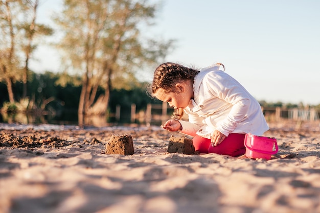 A girl plays with sand on a sandy beach on the river Bank during sunset.