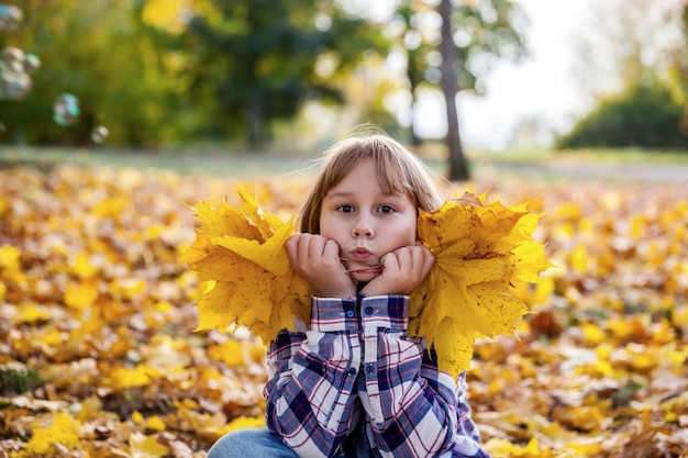 女の子は公園で黄色い紅葉で遊ぶ