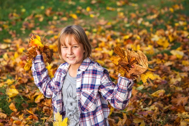 Girl plays with yellow autumn leaves in the park