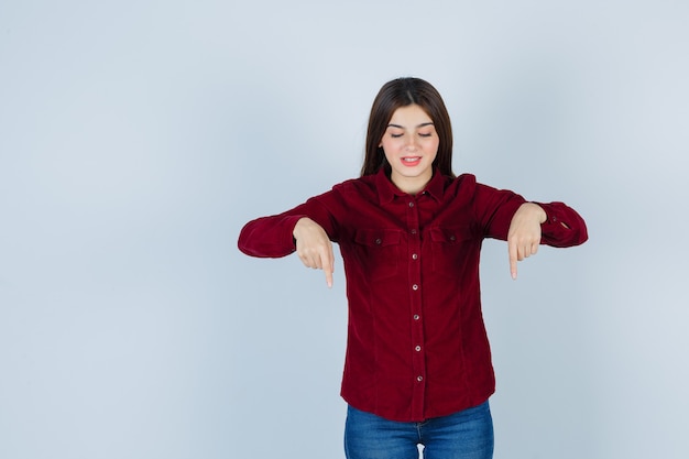 girl pointing down in burgundy blouse and looking cheerful