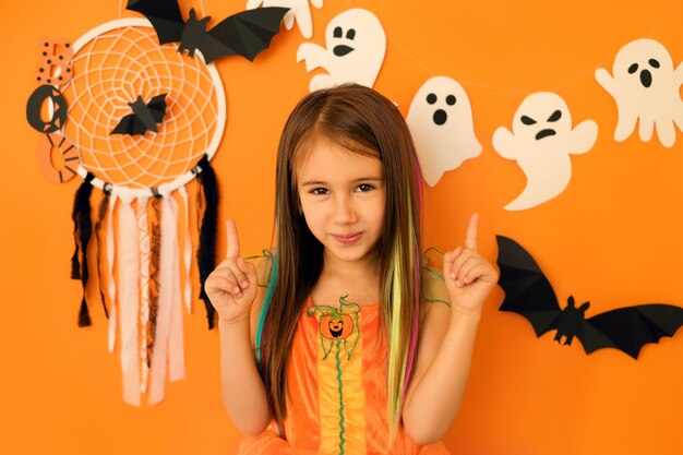 Girl pointing with index fingers upwards at copy space over studio halloween background