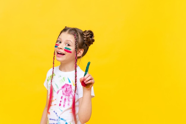 소녀는 위쪽을 가리킨다 노란색 외진 배경에 페인트로 얼룩진 아이 어린이를 위한 그리기 과정 어린이 창의력 개발