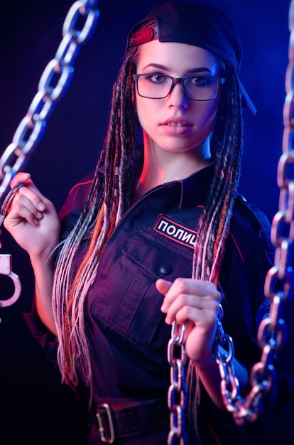 A girl in a police uniform with dreadlocks in neon light with chains and handcuffs English translation the police