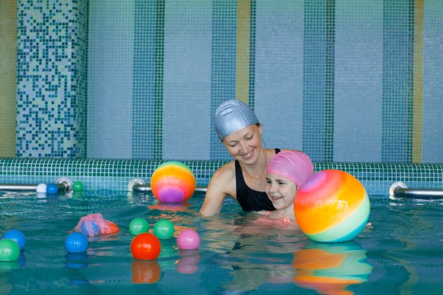 A girl in the pool with her mom collects colored balls