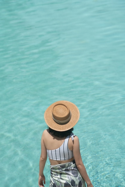 Photo girl posing near the pool in a fashionable swimsuit with pool reflect in the background / summer activity