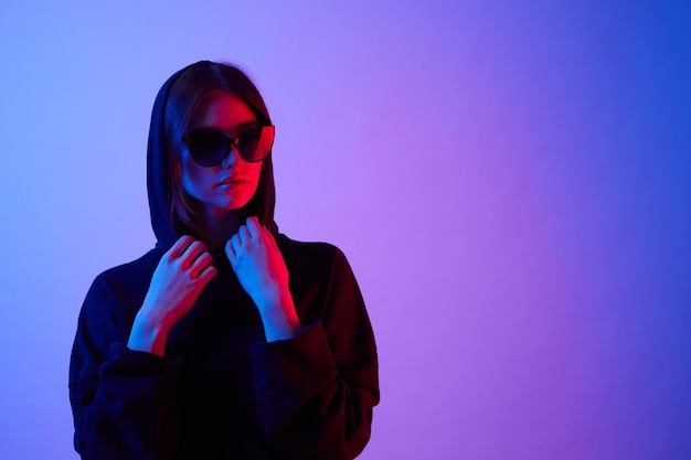 Girl posing in a trendy neon light Woman in sunglasses and hoodie with colorful light effects