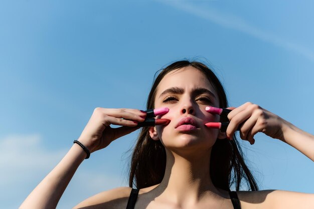 Girl posing with pink lips and lipsticks on blue sky