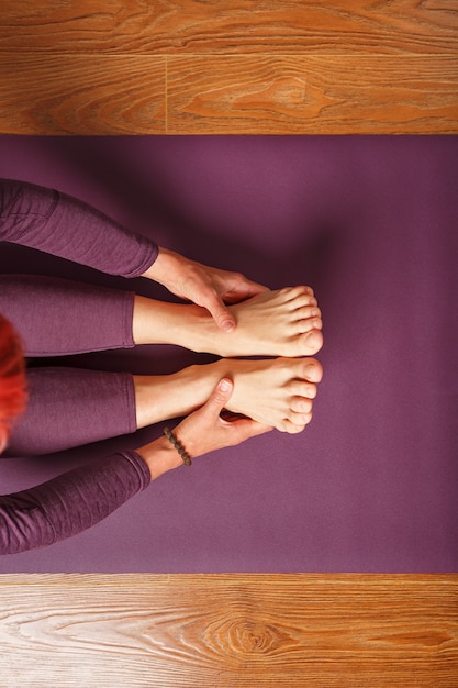 Girl practicing yoga leaning forward sitting, feet forward-paschimottanasana pose, training on a lilac mat
