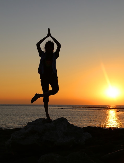 Girl Practicing Yoga at sunset on sea shore