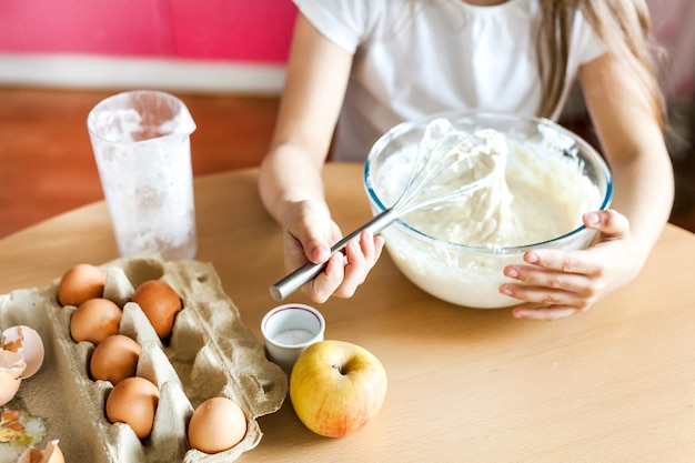 女の子は朝食を準備し、ベーキングし、小麦粉、牛乳、卵、パンケーキのボウルでかき混ぜ、子供たちは母親を助け、家族の朝食、料理