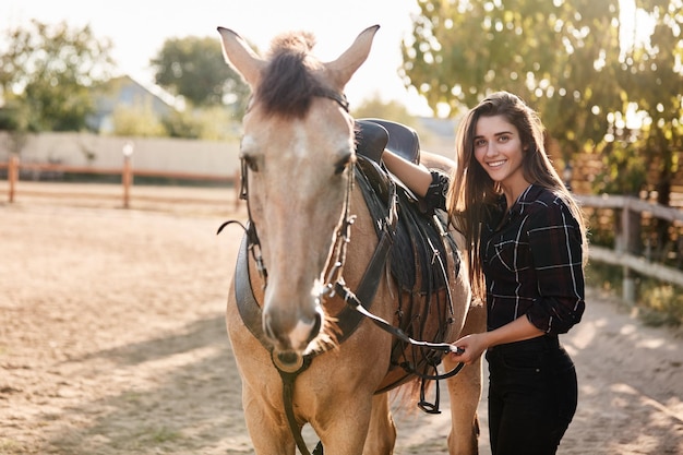 Girl prepare her horse for ride on racetrack Cheerful female jo