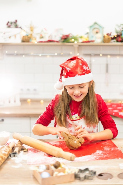 A girl prepares dough for gingerbread cookies in a red hat in the kitchen