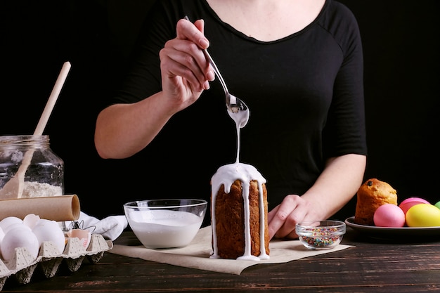 La ragazza prepara la cottura pasquale, spalma la torta con glassa e spruzza con polvere colorata