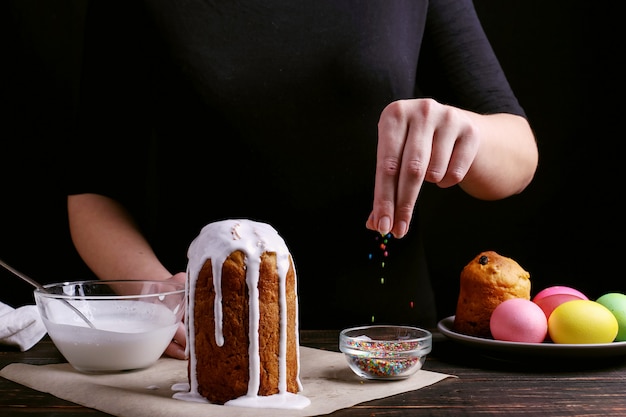 소녀는 부활절 제빵을 준비하고, 착빙으로 케이크를 바르고 착색 된 파우더로 뿌립니다.