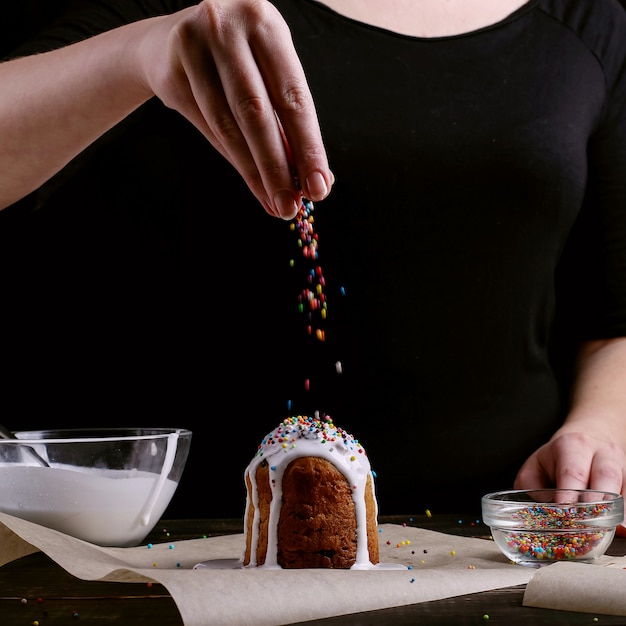 Photo the girl prepares easter baking, smears the cake with icing and sprinkles with colored powder