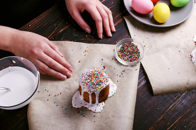 The girl prepares Easter baking, smears the cake with icing and sprinkles with colored powder