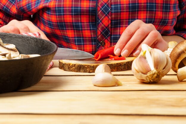 The girl prepares food. Close-up of female hands cutting hot red pepper on a round board.