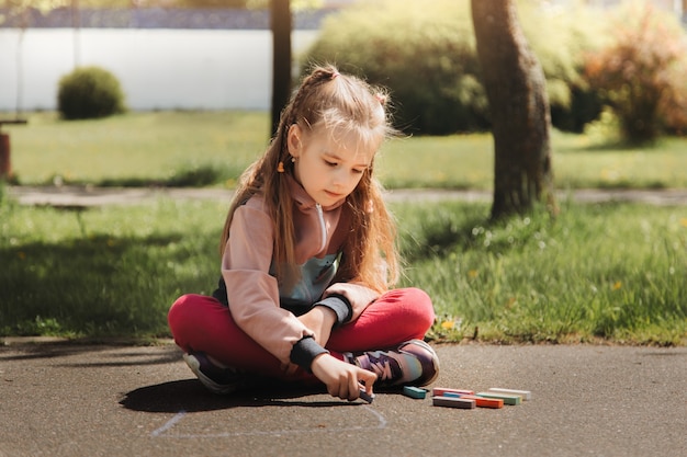 Girl preschooler draws with chalk on the asphalt in summer in the park