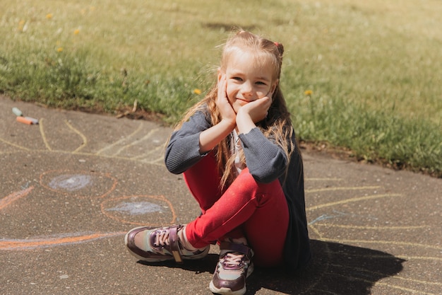 Photo girl preschooler draws with chalk on the asphalt in summer in the park