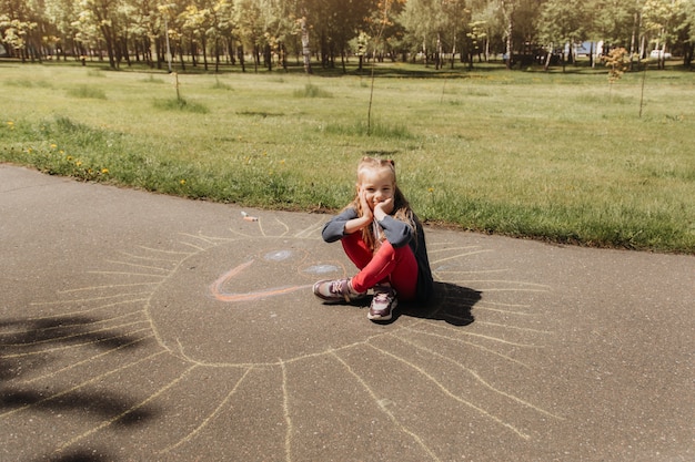 写真 未就学児の女の子が公園で夏にアスファルトにチョークで描く