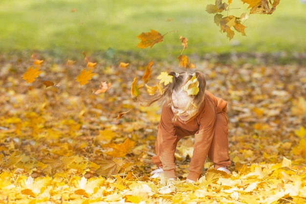 사진 여자 미취학 아동은 가을의 노란 잎을 가지고 놀고 가을의 따뜻한 계절에 그것들을 던집니다