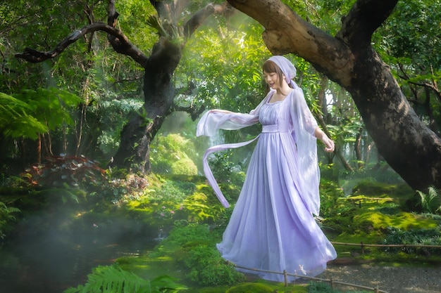 Girl in a princess dress is in a mysterious deep forest with trees flowers and waterfalls in the bac