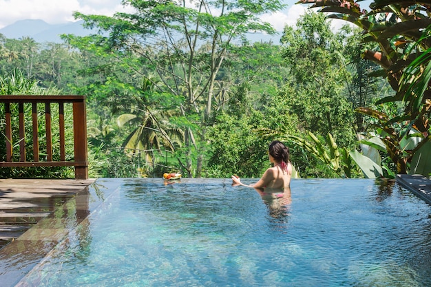 Photo girl in a private pool in bali admires a beautiful view of the palm trees.