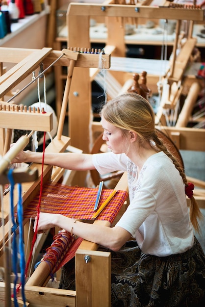 Девушка в процессе производства текстиля ручной работы на ткацком станке.