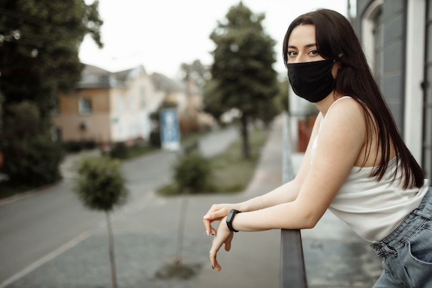 Girl in a protective mask on a balcony looks at an empty city