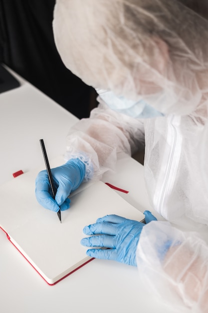 Girl in protective suit, blue rubber gloves, medical mask draws in sketchbook