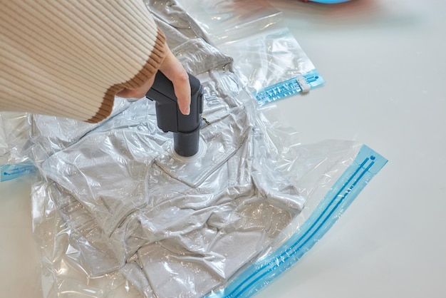 The girl pumps out air with a vacuum cleaner from a vacuum bag\
with clothes the concept of storage and transportation of clothing\
things space saving seal bag