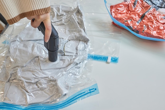 The girl pumps out air with a vacuum cleaner from a vacuum bag\
with clothes the concept of storage and transportation of clothing\
things space saving seal bag