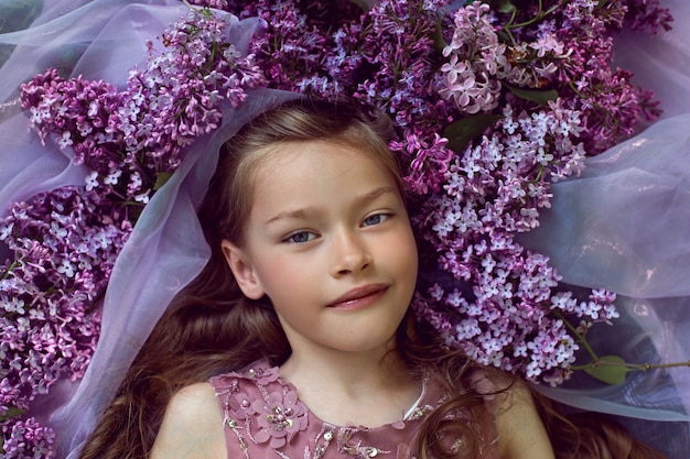 Ragazza in un abito floreale viola si trova tra i fiori di lillà