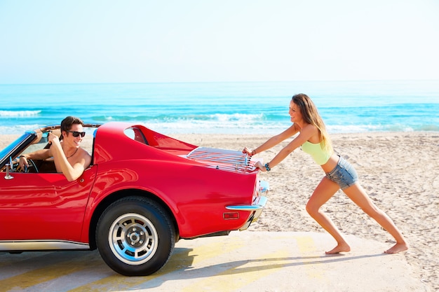 Ragazza spingendo una macchina rotta sulla spiaggia ragazzo divertente