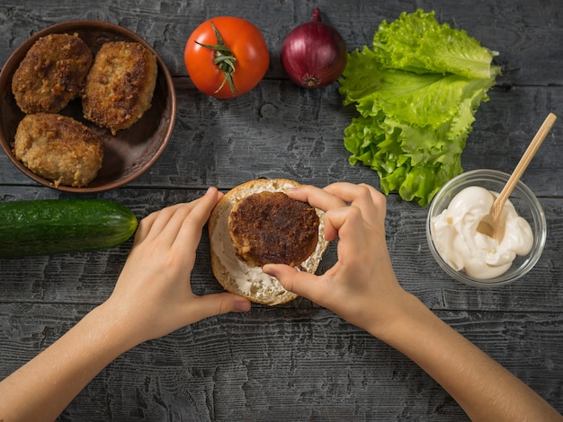 The girl puts the cutlet on a bun with sauce for cooking hamburger.