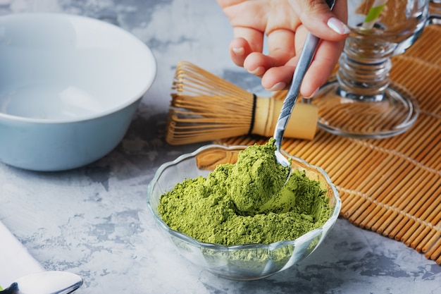 Photo girl puts a teaspoon of green tea powder in a bowl. matcha green tea powder, whisk and bowl.