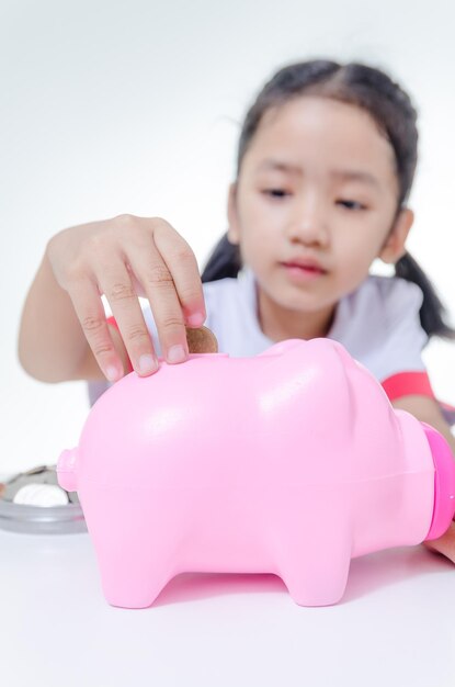 Girl putting coins in piggy bank against white background