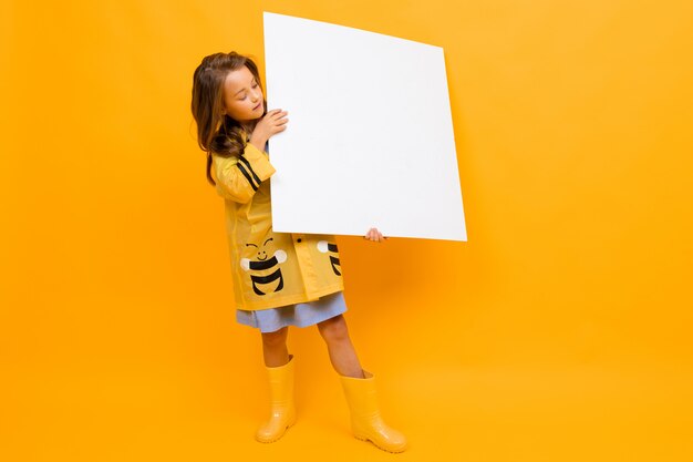 Girl in a raincoat holds a banner mockup with blank space on a yellow background
