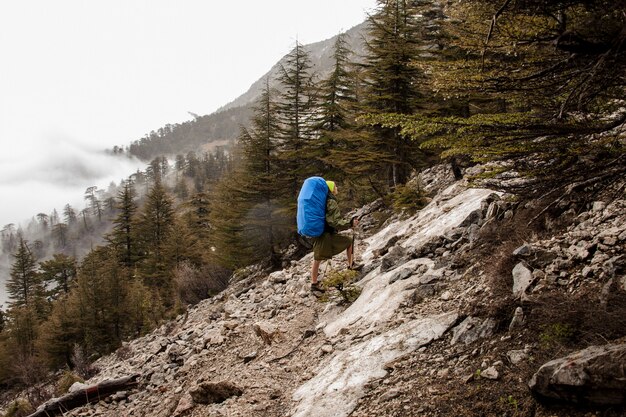 Girl in the raincoat walking up the rock with hiking backpack and sticks